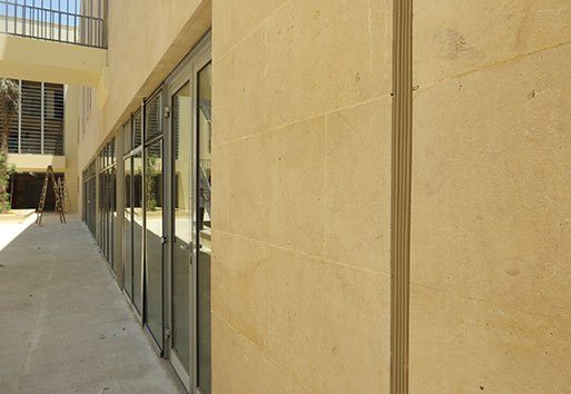 An up close view of the side of a yellow tinted wall on the exterior of a building, including glass doors and a ladder in view.