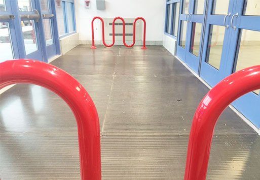 The Nystrom product, eleGRIL, is displayed on the entrance flooring of a public school, surrounded by two curvy rails and blue doors.