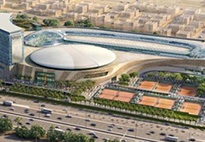 An aerial view of Kuwait Tennis Federation headquarters, surrounded by city life, including a highway and large buildings and greenery.